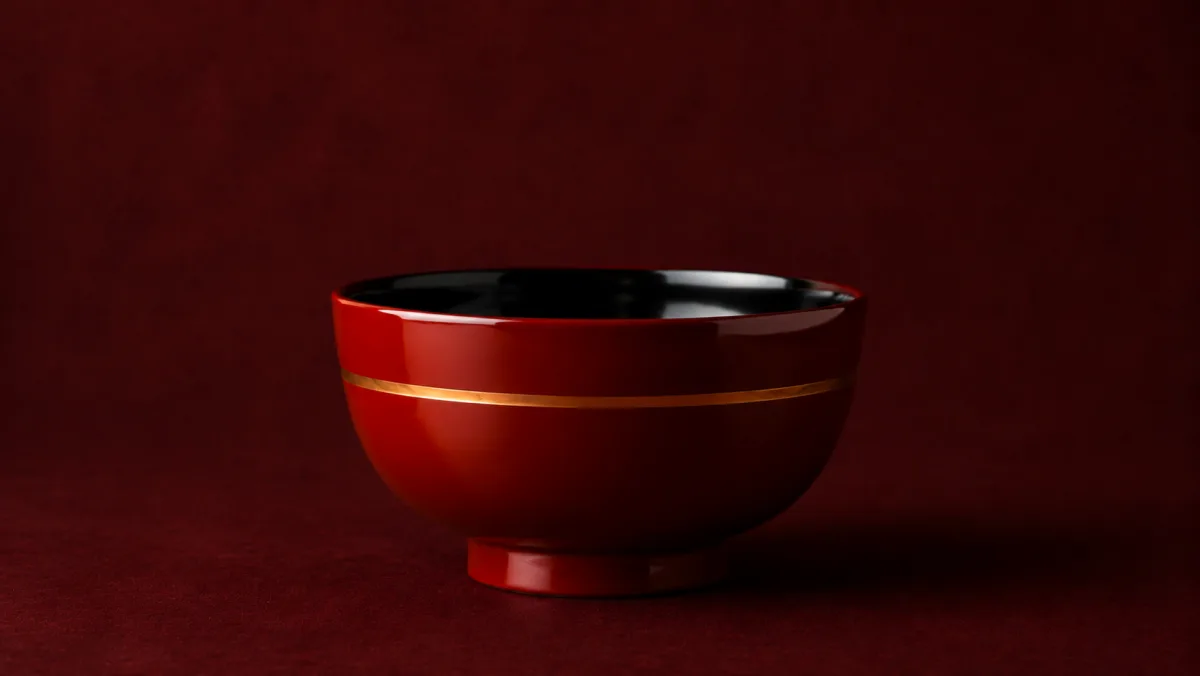 A vermilion lacquer bowl with a black interior, a fine gold band and a turned foot.